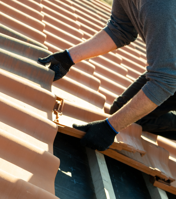 Person wearing gloves installing or repairing terracotta roof tiles on a sloped roof as part of roofing restoration in Colorado Springs.