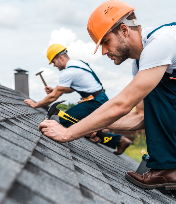 Two construction workers in hard hats install shingles on a roof, representing roofing work in Colorado Springs.