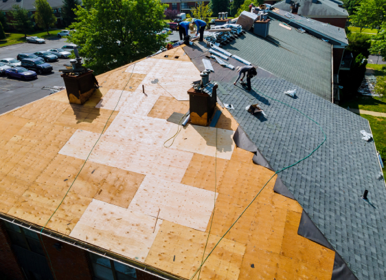 Several workers restore a large Colorado Springs roof, installing new shingles with tools and materials scattered across exposed plywood.