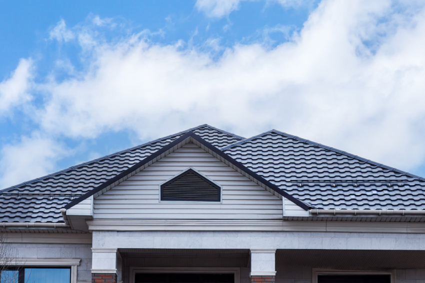 Empty unfurnished loft mansard room interior with wooden columns and wet concrete floor on roof level in black and whote style color A close-up of a gray, wavy metal roof and attic vent, showcasing exterior home restoration in Colorado Springs under a cloudy sky.