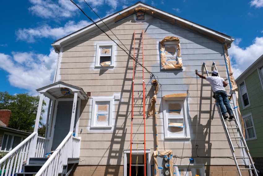Empty unfurnished loft mansard room interior with wooden columns and wet concrete floor on roof level in black and whote style color A person stands on a ladder painting a two-story house in Colorado Springs, prepping for exterior restoration and roofing work.