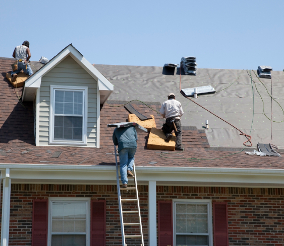 Three workers install new shingles on a brick house roof in Colorado Springs, restoring the exterior under a clear sky.