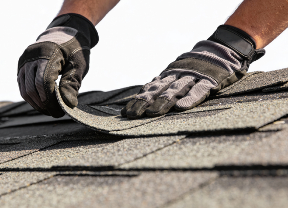 A person in protective gloves installs asphalt shingles on a Colorado Springs roof, part of local exterior home restoration work.